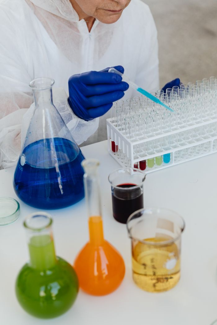 Scientist in protective gear filling test tubes with colorful liquids in a lab.